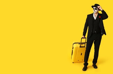 Young man with luggage dressed for Mexico's Day of the Dead (El Dia de Muertos) on yellow background with space for text