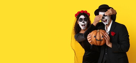 Young couple dressed for Halloween holding pumpkin on yellow background with space for text