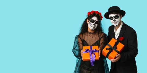 Young couple dressed for Mexico's Day of the Dead (El Dia de Muertos) holding gifts on light blue background with space for text