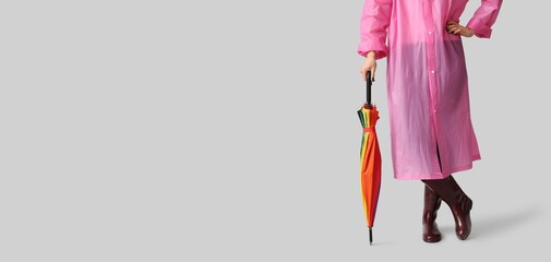 Young woman in raincoat and with umbrella on grey background with space for text