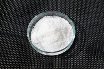 Common edible salt of white color in a petri dish, dark background. Sodium chloride