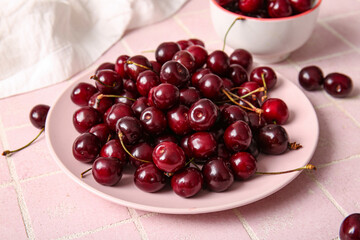 Plate and bowl with sweet cherries on pink tile table