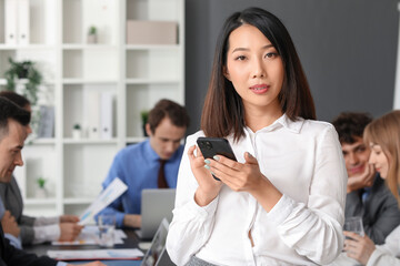 Female Asian business consultant with mobile phone in office