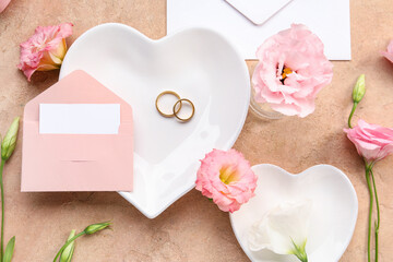 Composition with envelope, blank card, wedding rings and eustoma flowers on beige background, closeup