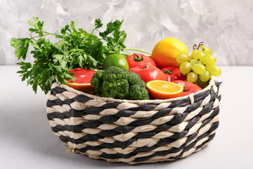 Wicker bowl with different fresh fruits and vegetables on white table