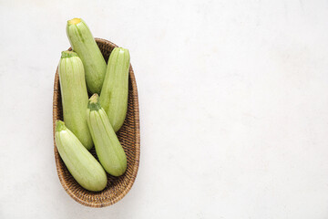 Wicker bowl with fresh green zucchini on light background