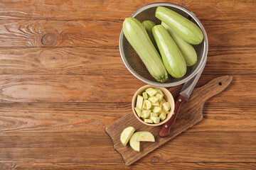 Colander and bowl with fresh green zucchini on wooden background