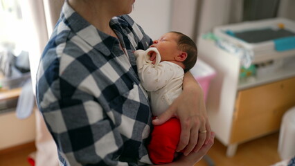 Newborn baby gazing up at mother, nestled comfortably in her arms. The bedroom setting adds to the...