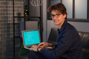 Happy young businessman sitting on sofa in office and working with laptop