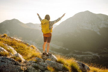 A joyful hiker enjoys the breathtaking view from a mountain summit during a sunny afternoon in the serene foothills. Nature, active life, travel.