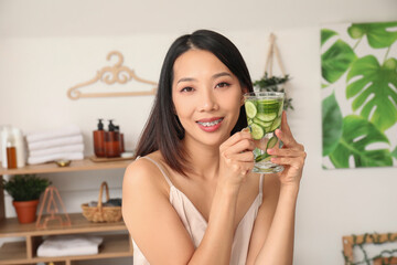 Young Asian woman with glass of cucumber water at home
