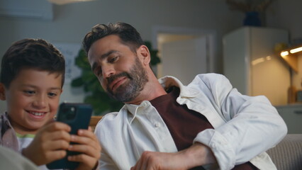 Fototapeta premium Serious boy playing mobile phone resting sofa closeup. Funny father looking son