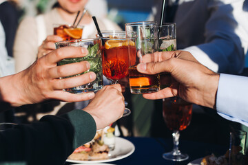 Group of guests celebrate and raise glasses, cheering with alcohol glasses with wine and champagne on corporate christmas open air summer birthday party event or wedding celebration, luxury event