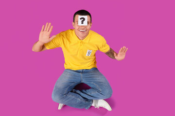 Young man with paper question mark on his forehead against purple background