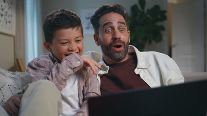 Family engrossed funny movie relaxing at home closeup. Daddy son with laptop