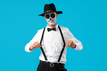 Young man with painted skull on blue background. Mexico's Day of the Dead (El Dia de Muertos) celebration