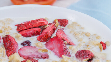 Close up of a white bowl of healthy cereal and dry strawberry with milk placed colorful napkin. Side view of white milk in bowl with cornflake, fruit with. Slow motion. Macro photography. Pabulum.