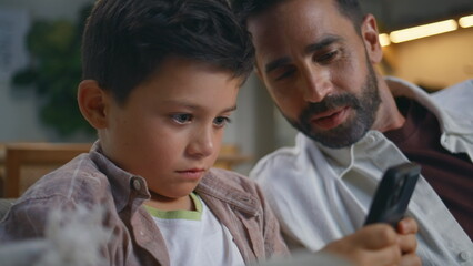 Father son playing cellphone game at evening home closeup. Man kid inonline