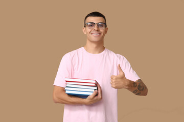 Handsome young man with books showing thumb-up on beige background
