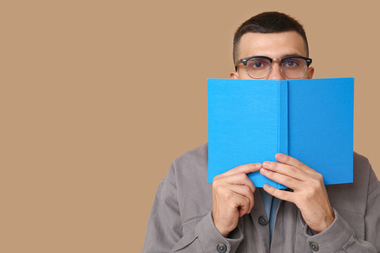 Young man covering face while reading book on beige background
