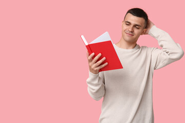Thoughtful young man reading book on pink background