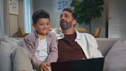 Dad son viewers laughing looking amusing film on laptop at cozy sofa closeup