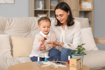 Cute little daughter doing nails of her beautiful mother at home