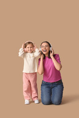 Beautiful mother with her cute little daughter in headphones listening music on brown background
