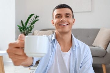 Smiling man offering cup of coffee in living room, closeup