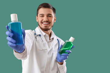 Young male dentist with bottles of mouthwash on green background. Dental care concept