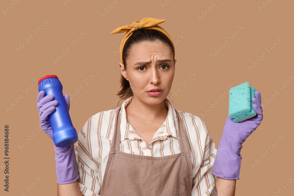 Canvas Prints Portrait of tired young housewife in apron with detergent and sponge on brown background