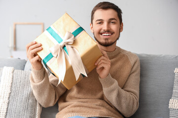 Young man with gift sitting on sofa at home