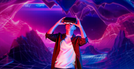 Man with casual cloth playing video game while wearing VR headset and standing at abstract background. Smart asian gamer using augmented reality technology celebrating for winning the game. Ingenuity.