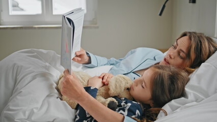 Lying mom child reading at cozy bed closeup. Woman girl enjoying fairy tale