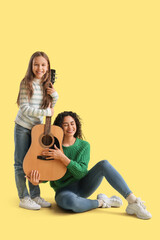 Young woman and girl with acoustic guitar on yellow background