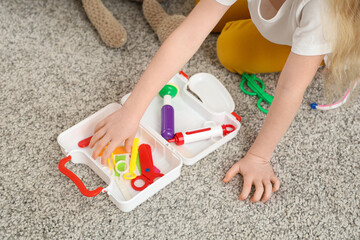 Little girl with toy first aid kit on floor at home