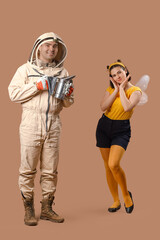 Male beekeeper with smoker and woman in bee costume on brown background