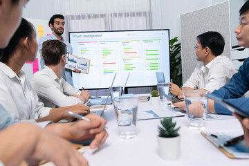 Project manager communicate and collaborate with team using project management software display on monitor, tracking progress of project task and making schedule plan at meeting table. Prudent