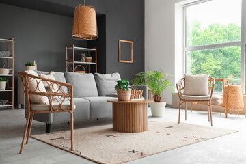 Wicker armchairs, sofa and round wooden table in interior of living room