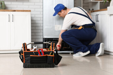 Male worker with tools repairing refrigerator in kitchen