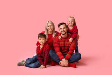 Happy family with children in winter clothes sitting on pink background