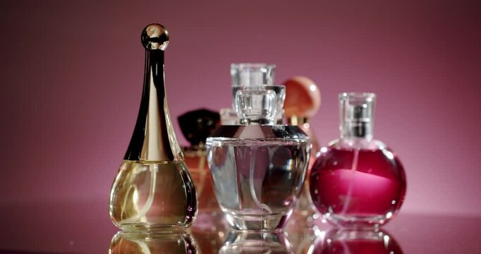 A collection of elegant perfume bottles displayed on a glass surface with a pink background. The assortment of fragrances showcases luxury and sophistication, ideal for beauty and fashion themes.
