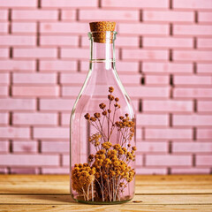 Dried flowers in glass bottle on wooden table and brick wall background