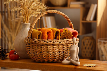 Wicker basket with folded stylish clothes and autumn decorations on table in living room, closeup