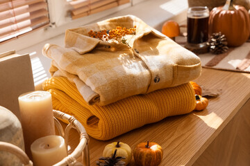 Stack of stylish clothes with autumn decorations on commode near window in living room
