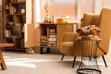 Stack of stylish clothes with autumn decorations on stool near open commode in living room