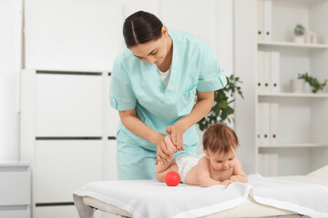 Obraz premium Cute little baby getting feet massage with ball from happy professional therapist on couch in clinic