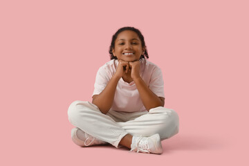 Emotional African-American girl sitting on pink background
