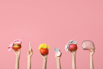 Women holding funny pumpkins with facial masks, cosmetics and bag on pink background