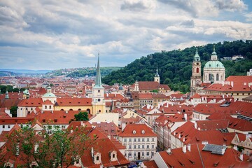 Fototapeta premium This stunning cityscape of Prague showcases charming red-roofed buildings and historic churches, capturing the essence of the citys architectural beauty against a captivating cloudy sky.